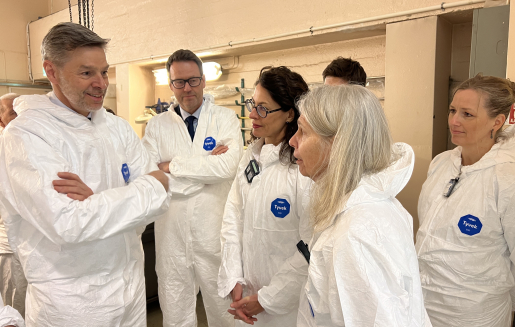 NNSA Administrator Jill Hruby listens to Nils Morten Huseby and Nils Bøhmer. All of them are dressed in white clean suits but their heads are uncovered.