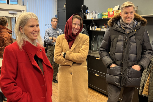 Administrator Hruby laughs during a presentation. Two other people are next to her, smiling. They are all dressed in coats.