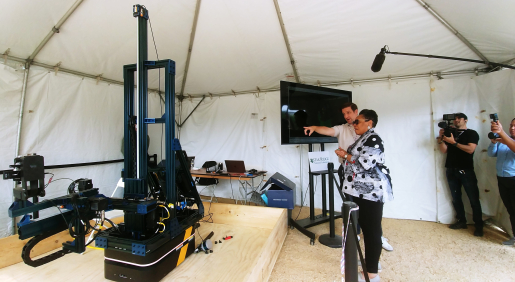 Two people looking at equipment in the ORNL tent display, with two other people looking on with cameras.