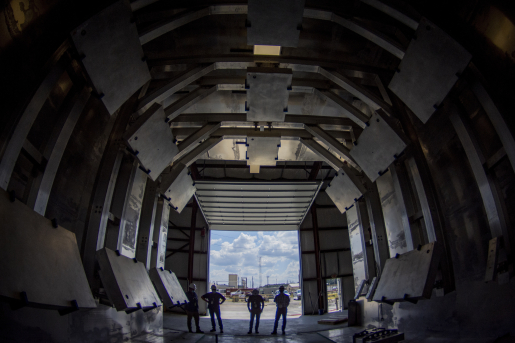 Four people standing with their backs to the camera standing inside dark facility.