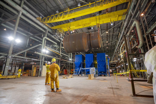 Two workers observing large metal cast being lifted in the air.