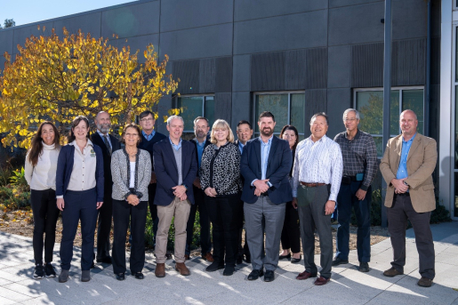 A group of people stand together outside in front of a building for a group photo.