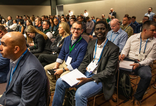 Two people smiling at the camera, surrounded by other conference attendees.