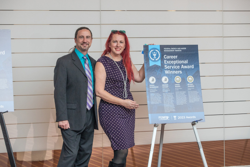 Two people posing by a poster.