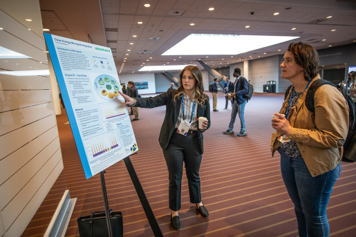 One person gesturing at a poster while another listens.