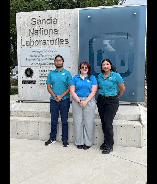 Three people standing in front of Sandia National Laboratory sign