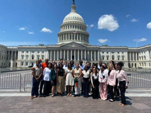 A group of student interns dressed in business casual clothes stand in front of the Capitol Building in Washington, D.C.
