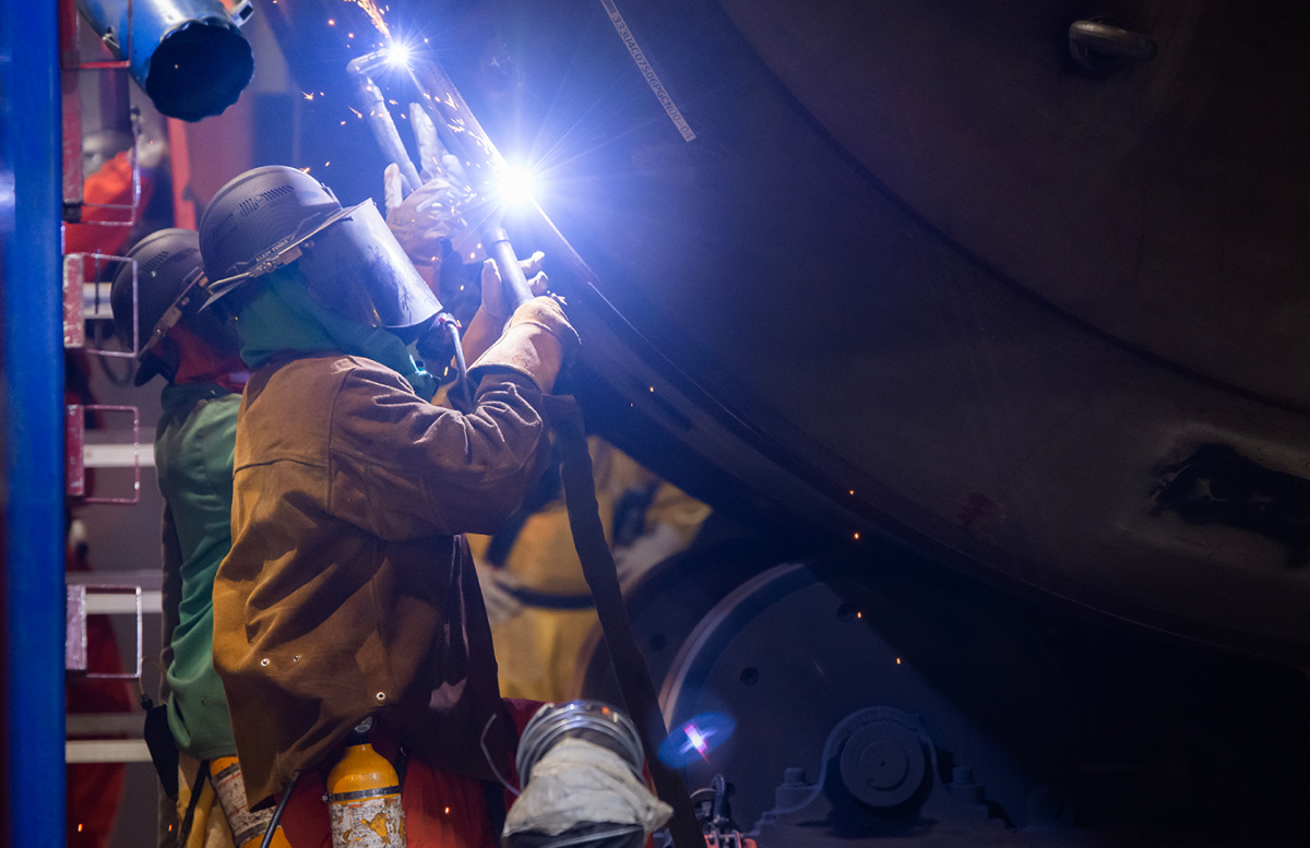 A welder wearing protective gear working inside a facility building