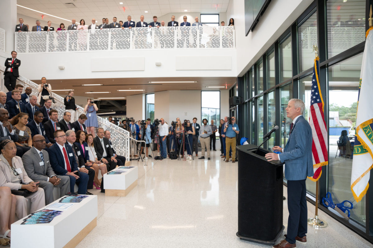 A photo showing a speaker behind a podium speaking to a large group of people.