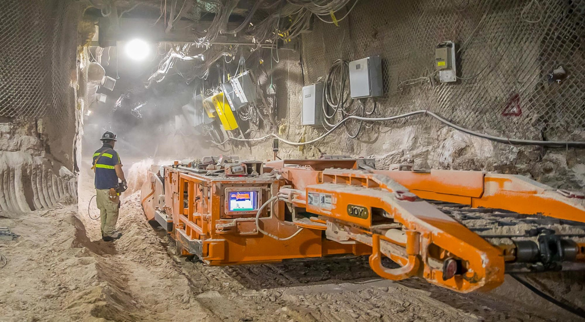 A photo of a worker standing next to a large piece of underground mining equiptment.