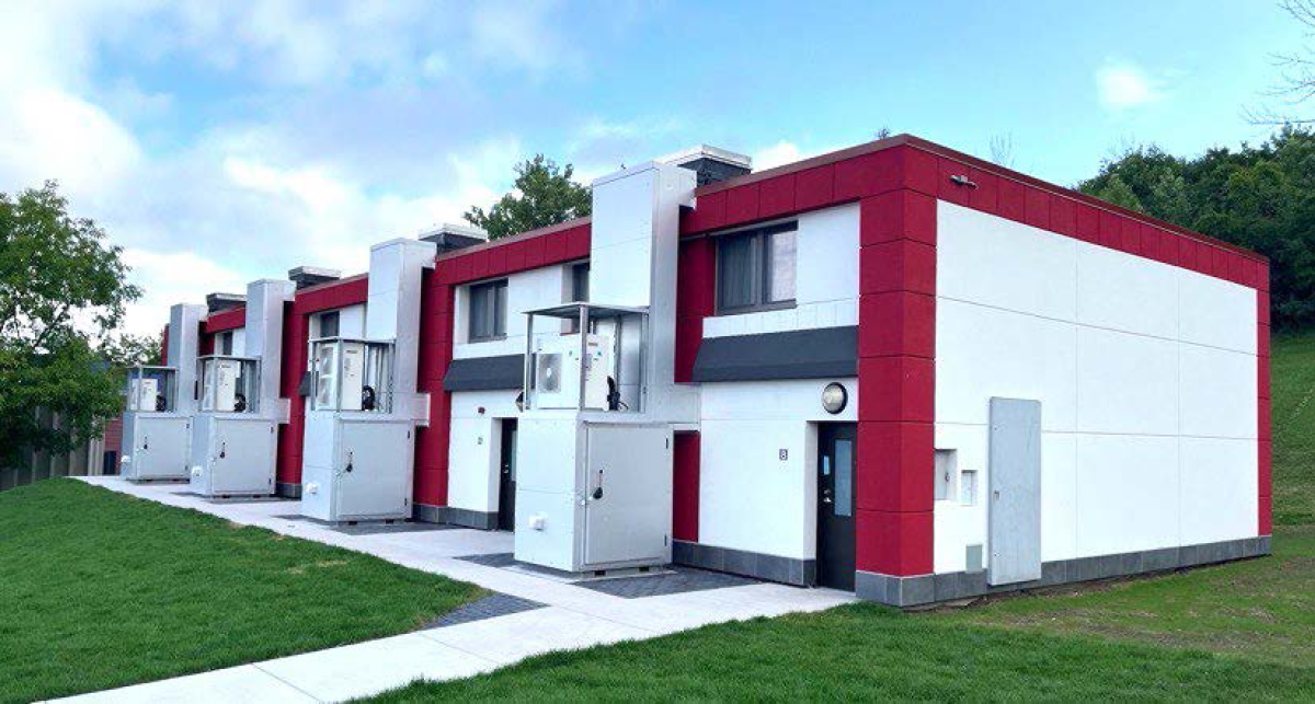 A row of block-style housing with a sidewalk in front of it and the sky showing above.