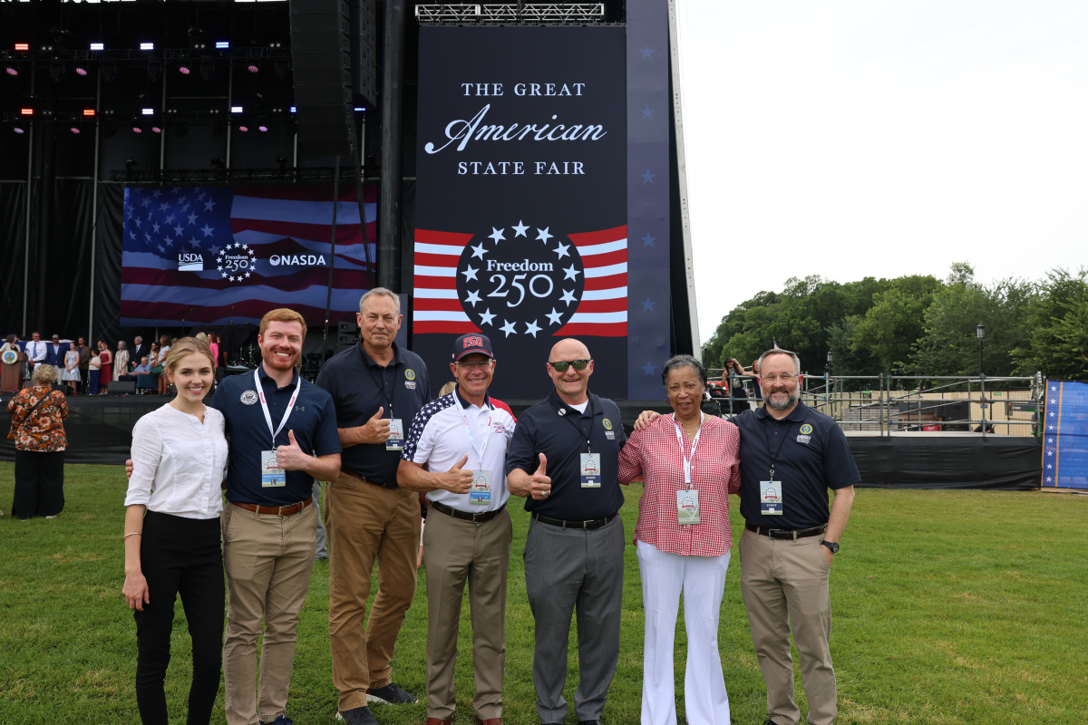 Group photo in front of The Great American State Fair Freedom 250 Flag