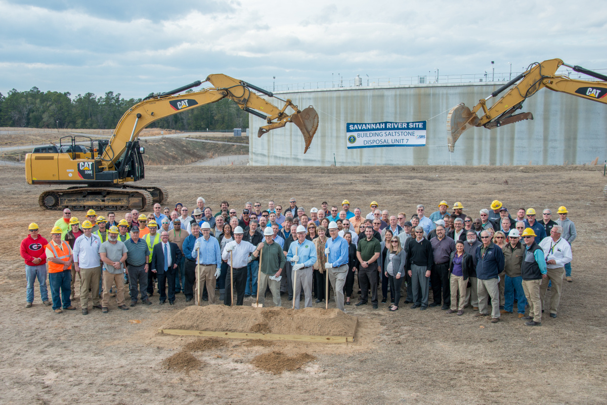A large group of people posing for a photo on a dirt site at SRS