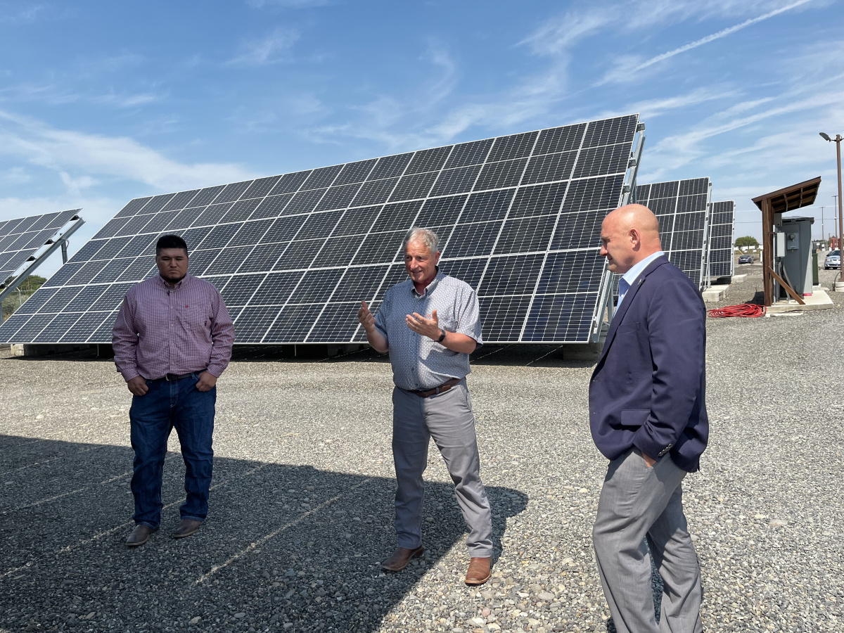 Three professionals standing by taking a tour of a site with solar panels behind them