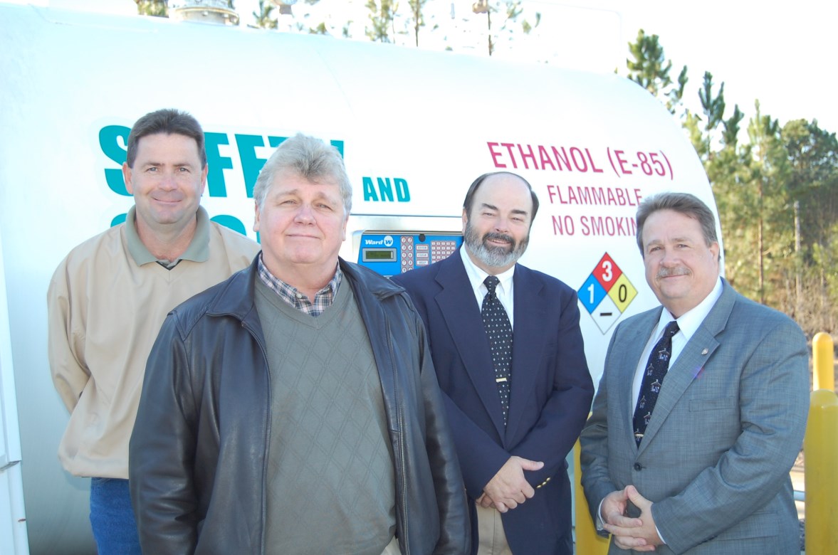 Photo of four men standing in front of a white ethanol (E85) fuel tank.