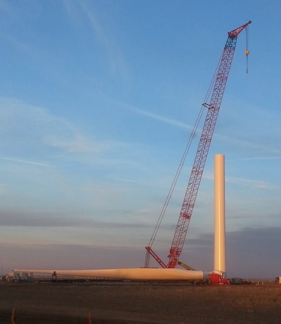 Photo of a large red crane standing over two large yellow wind turbine pieces.