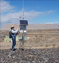 Photo of a man in a hat adjusting controls on a ground antennae with solar panels on it.