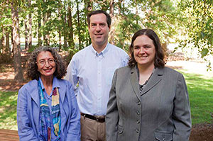 Photo of two women and a man standing outside in front of trees.