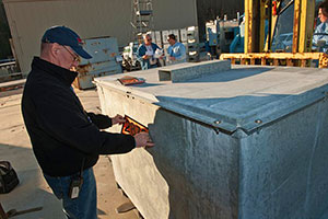 Photo of a man putting a numbered decal on a large metal container.