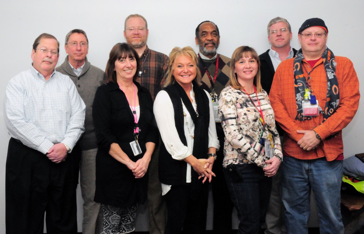 Photo of nine people standing together; three woman are in the front row and six men are in the back row.