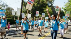 Photo: Lindsay McCord Photo of people marching in a parade with signs, wearing matching shirts.