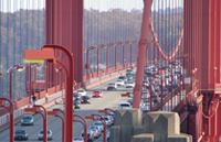 Daytime photo of a bridge with cars on it, and a roadway light in the left foreground.