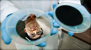 NREL research scientist Hao-Chih Yuan displays silicon wafers before (left) and after (right) the wet-chemical etching process that creates award-winning "black silicon" solar cells. Photo by Dennis Schroeder, NREL/PIX 17852 Photo of a researcher holding two disc-shaped solar cells, one that is black and one that is reflective, showing his face.