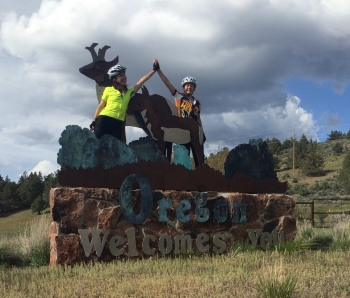 Rachel Woods-Robinson and Elizabeth Case, the ladies of Cycle for Science, high-five on top of the "Welcome to Oregon" sign. | Photo courtesy of Cycle for Science. Rachel Woods-Robinson and Elizabeth Case, the ladies of Cycle for Science, high-five on top of the "Welcome to Oregon" sign. | Photo courtesy of Cycle for Science.