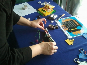 Volunteer Alison Mize demonstrates how to build an electrical circuit using a string of lights and battery at the Vehicle Technologies Program booth at the 2011 Solar Decathlon. | DOE photo, courtesy of April Saylor Volunteer Alison Mize demonstrates how to build an electrical circuit using a string of lights and battery at the Vehicle Technologies Program booth at the 2011 Solar Decathlon. | DOE photo, courtesy of April Saylor
