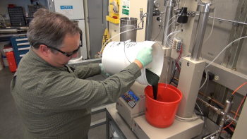 PNNL lab manager Todd Hart pours wet biomass into a bucket as he begins an experiment to convert the substance into biocrude oil. Photo Courtesy of PNNL. PNNL lab manager Todd Hart pours wet biomass into a bucket as he begins an experiment to convert the substance into biocrude oil. Photo Courtesy of PNNL.