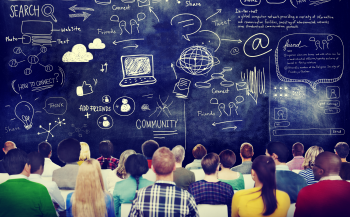 Photo of a group of people sitting in front of a giant chalkboard with lots of writing on it.