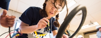 A student holds a screwdriver and she adjusts her project in the Collegiate Wind Competition
