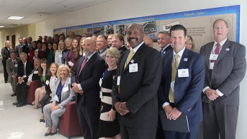 members of the chamber and DOE leaders pose by a wall display in DOEâs Forrestal Building highlighting the history, operations, and cleanup at the Paducah Gaseous Diffusion Plant.