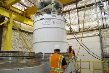 Operations technicians Larry Hampton and Gerardo Lazalde load a 4,855-pound transuranic waste package into a shipping container at the Idaho Site.