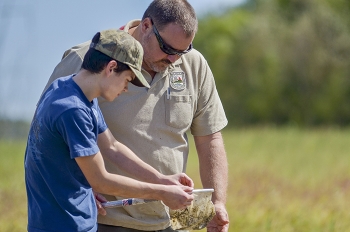 Tim Kreher with the Kentucky Department of Fish and Wildlife Resources assists Marshall County High School advanced placement physics student Tanner Hayes with environmental field work during his classâs visit.