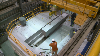 A worker looks on as a crane helps to remove a part of the nuclear reactor's shield block.