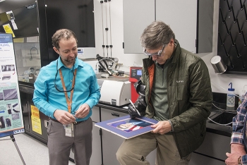 Secretary Perry tests the dexterity of glovebox gloves made with a Savannah River National Laboratory-developed nanomaterial by signing his autograph while SRNL Senior Scientist Dr. Jay Gaillard watches.