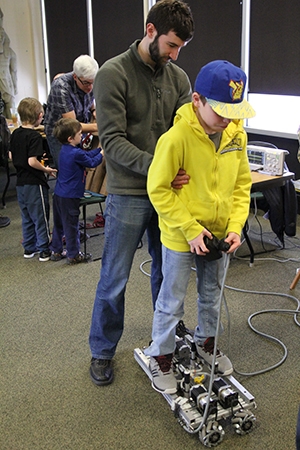 Fluor Idaho employee Chris Graham holds Ethan Herrera steady as he rides the "calcine crawler," a robotic device designed to sweep material out of a calcine tank.