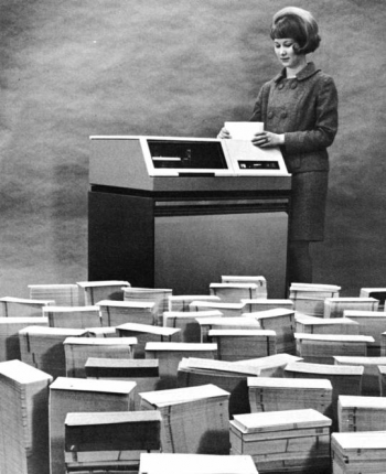 1964: A female employee at the Kansas City Plant loads data storing punch cards onto a disk drive.
