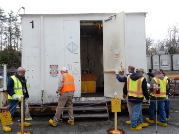 Workers prepare to install vents in drums of legacy transuranic waste in a closed, explosion-proof, high-efficiency particulate air-ventilated unit to ensure safety of workers and the environment.