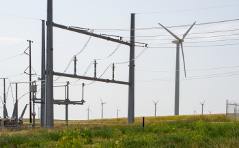 Electrical transmission lines in a field next to a wind turbine.