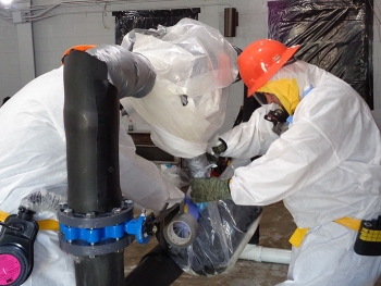 A new worker learns about asbestos abatement in a mock-up, which serves as a training ground before beginning work inside the Biology Complex.
