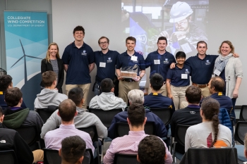 Students pose in front of a projector, one holding a trophy.