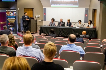 Director Campos leans on the podium and watches as the STEM education panel speaks.