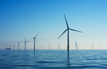 Many wind turbines in ocean and silhouetted against blue sky.
