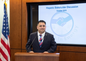 Director Campos stands at a podium and speaks to the audience. Behind him is the American flag on one side and the Equity in Energy logo on the other.