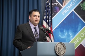Director Campos is speaking at a podium. Visible on the podium is the DOE seal. Visible in the background is the American flag.