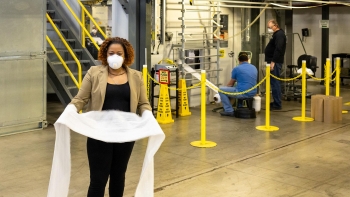 a woman holding some fabric, while wearing a mask