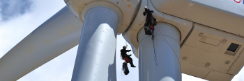 Two men hanging from a wind turbine as they work to prepare the turbine.