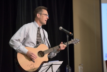 Photo of Eric Werling playing a guitar at a microphone during an event.